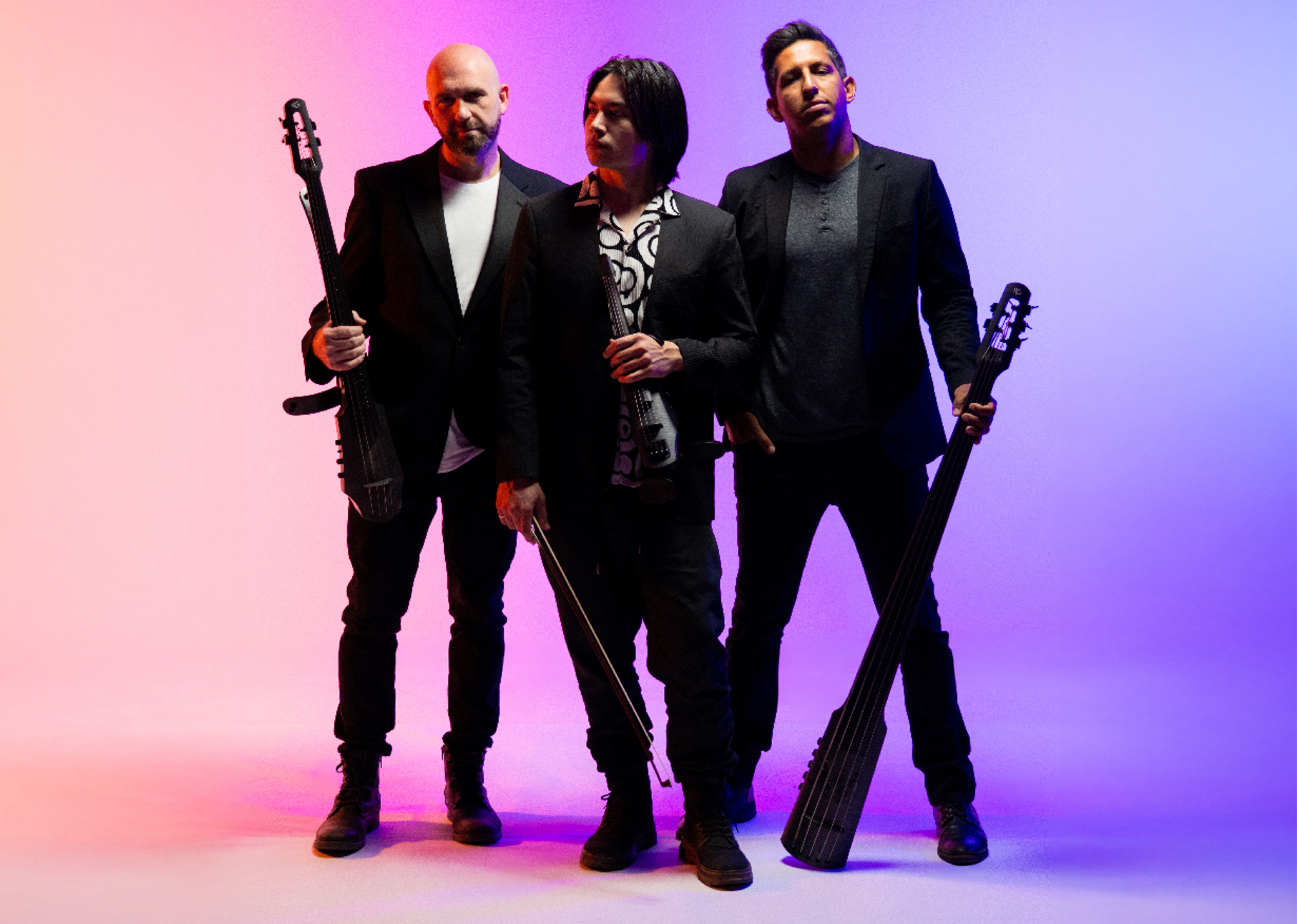 Three men holding instruments dressed in black jeans, boots and blazers on a purple and pink background